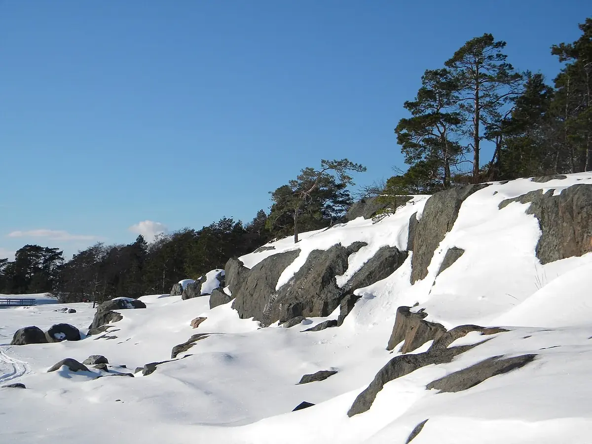 Snötäckt stenig kuststräcka med berg i dagen, nordisk vinter