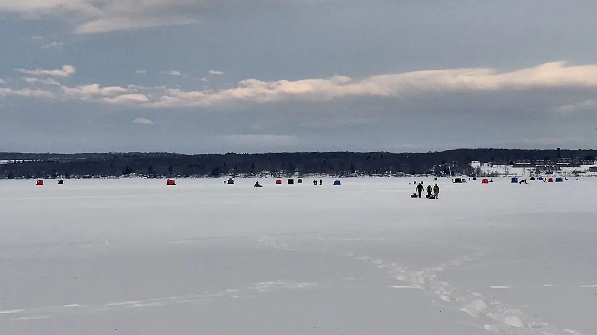Anglers pulling sleds out onto frozen Chautauqua Lake in New York on a January evening, with ice shelters spread across the lake
