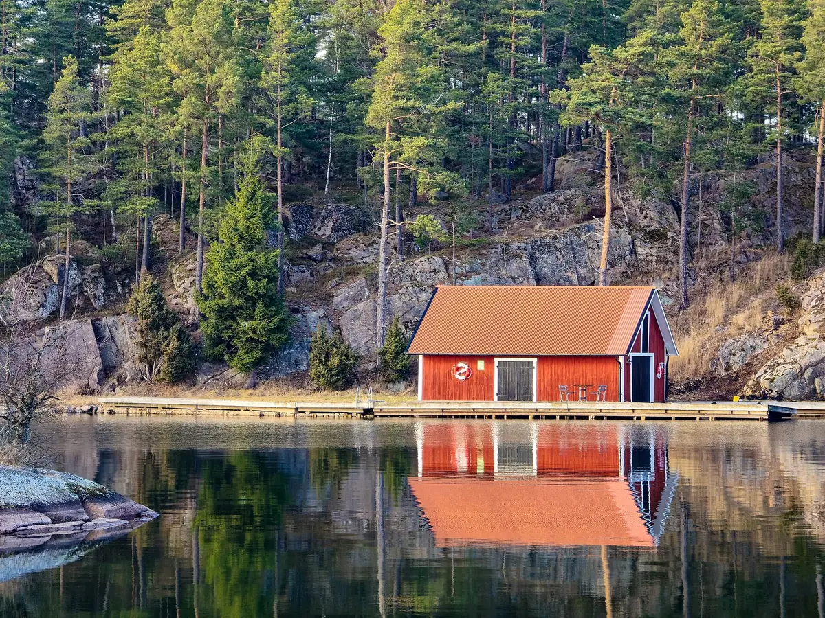 Ett rött båthus speglas i en spegelblank sjö, den sortens stilla morgon då ytvattnets temperatur avgör var fisken står.